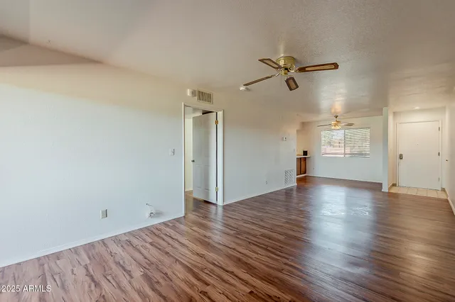 an empty room with wooden floor ceiling fan and windows