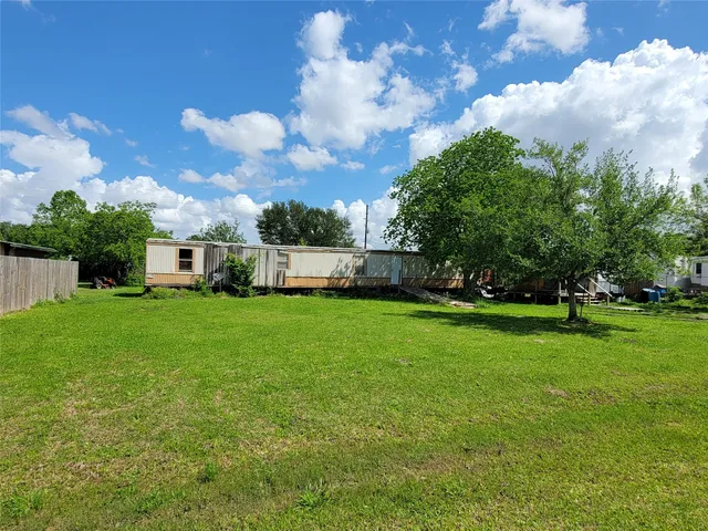 a view of a white house in front of a big yard with plants and large trees