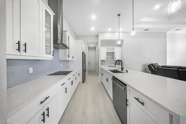 a large white kitchen with a stove a sink a refrigerator and white cabinets with wooden floor