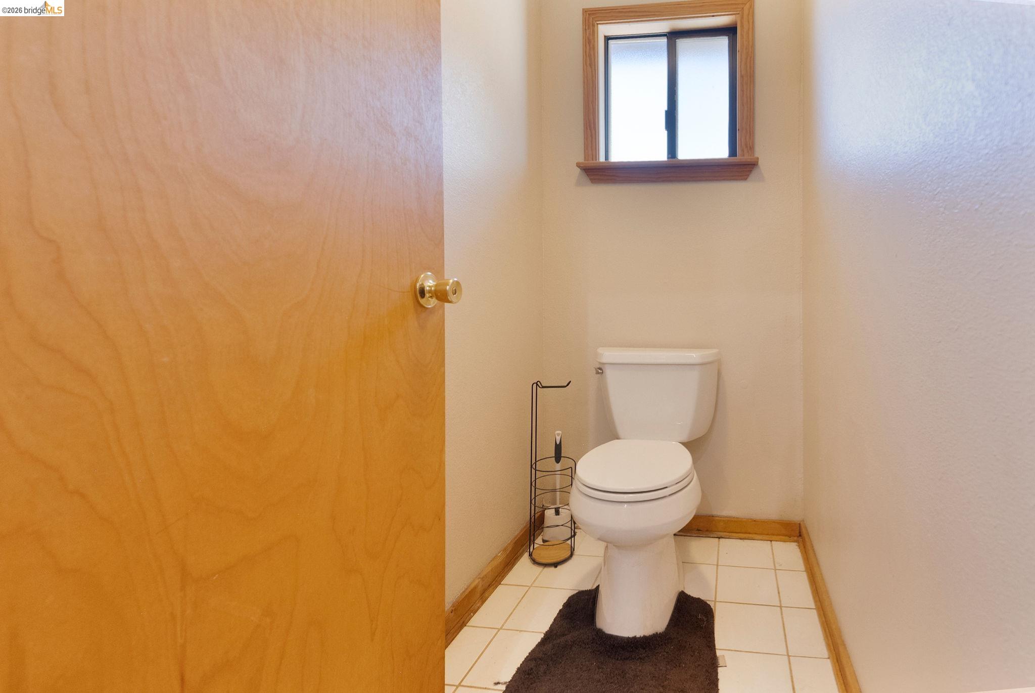 22963 Robertson Ranch Road Sonora, CA 95370 - Photo 55 of 90 Compact powder room featuring a single toilet, a wood-framed window, neutral painted walls, and light-colored tile flooring with wood trim