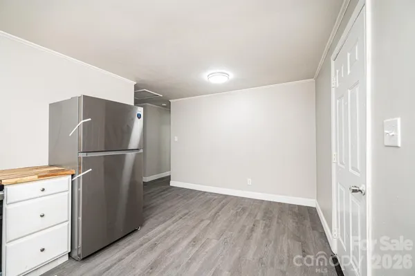 a view of an empty room with wooden floor and a kitchen