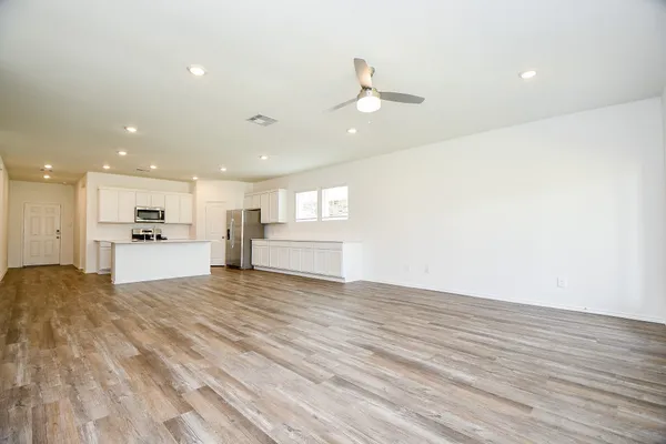 a view of an empty room with wooden floor and kitchen view