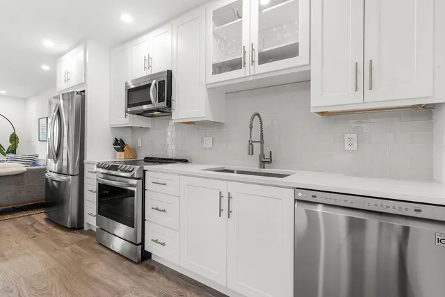 a kitchen with stainless steel appliances granite countertop white cabinets a sink a stove a refrigerator and microwave with wooden floor