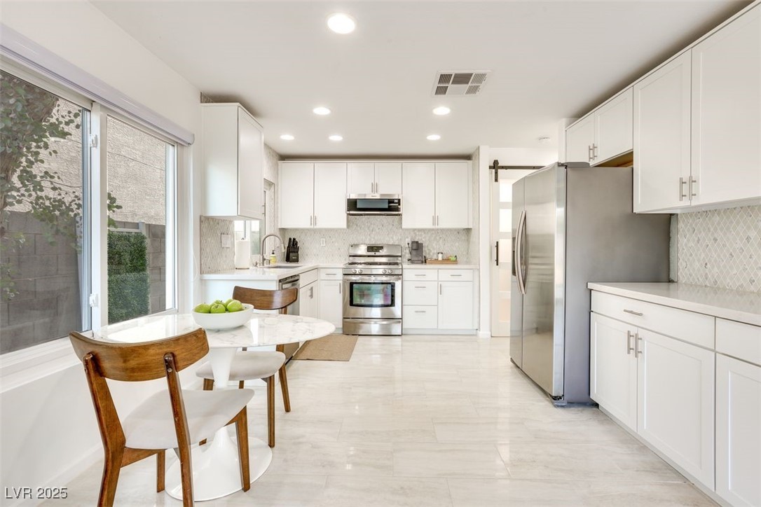 Kitchen with stainless steel appliances, backsplash, light countertops, white cabinetry, and a sink