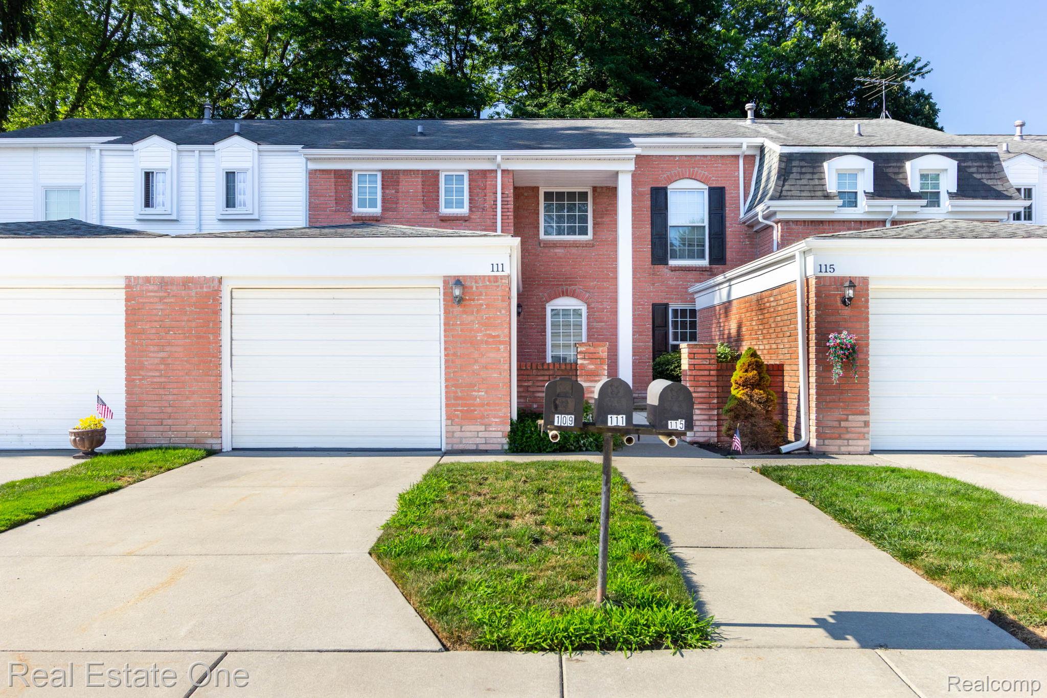 111 Manor Way Rochester, MI 48309 - Photo 1 of 36 Red brick facade townhome featuring white garage doors, a concrete driveway, and dormer windows