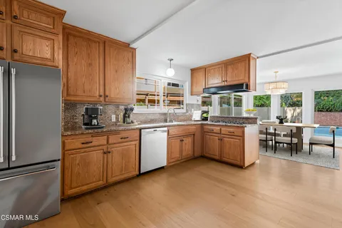 a kitchen with stainless steel appliances granite countertop a stove a sink dishwasher a refrigerator with white cabinets and wooden floor