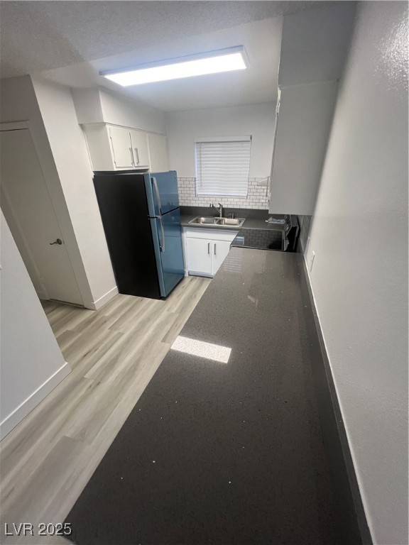 797 East Harmon Avenue, Unit 7 Las Vegas, NV 89119 - Photo 6 of 12 Kitchen featuring dark countertops, refrigerator, white cabinetry, light wood finished floors, and tasteful backsplash
