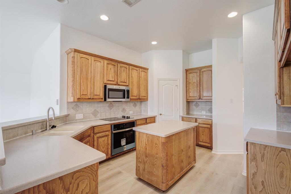 12405 Ark Road Frisco, TX 75035 - Photo 18 of 34 Kitchen featuring oven, light wood-style flooring, stainless steel microwave, decorative backsplash, and black electric cooktop