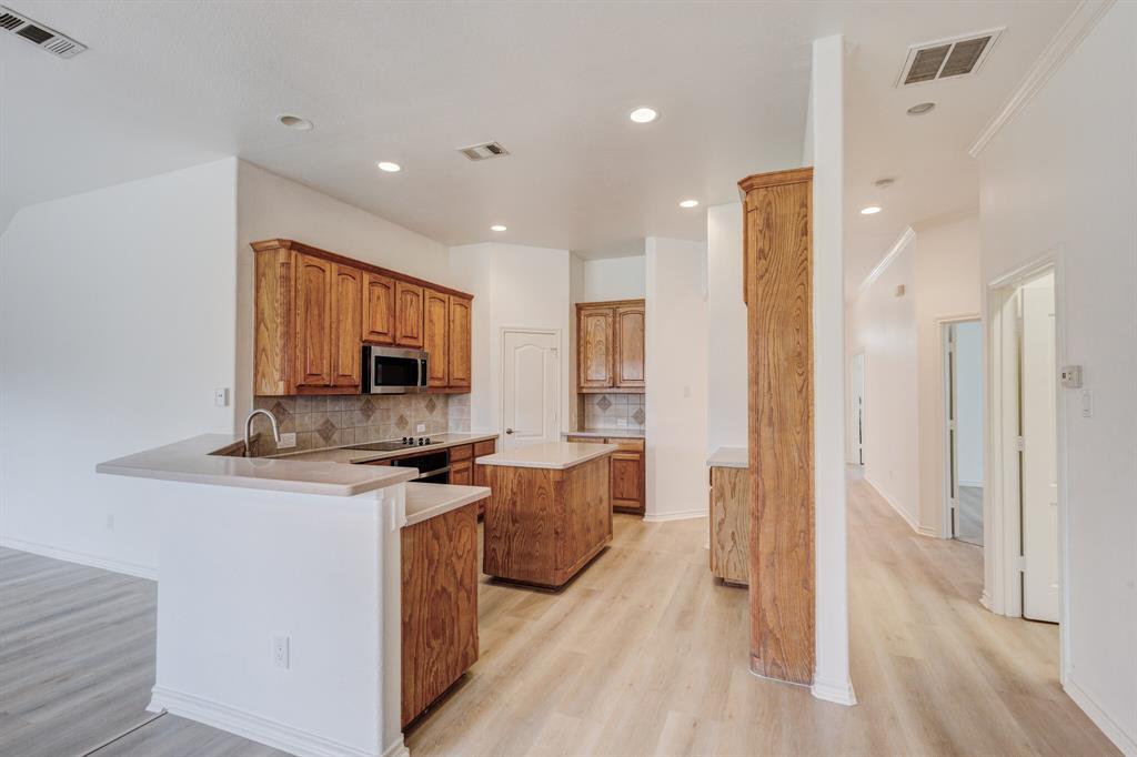 12405 Ark Road Frisco, TX 75035 - Photo 20 of 34 Kitchen with wood finish cabinets, a center island, decorative backsplash, light countertops, and a peninsula