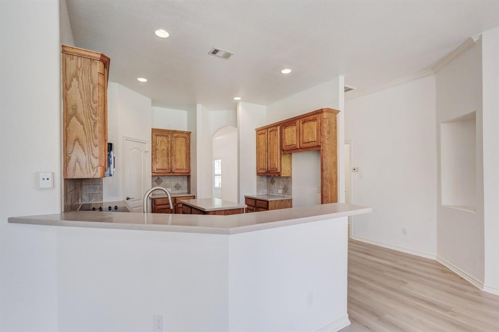 12405 Ark Road Frisco, TX 75035 - Photo 23 of 34 Kitchen with a peninsula, light wood-type flooring, backsplash, wood finish cabinetry, and a center island