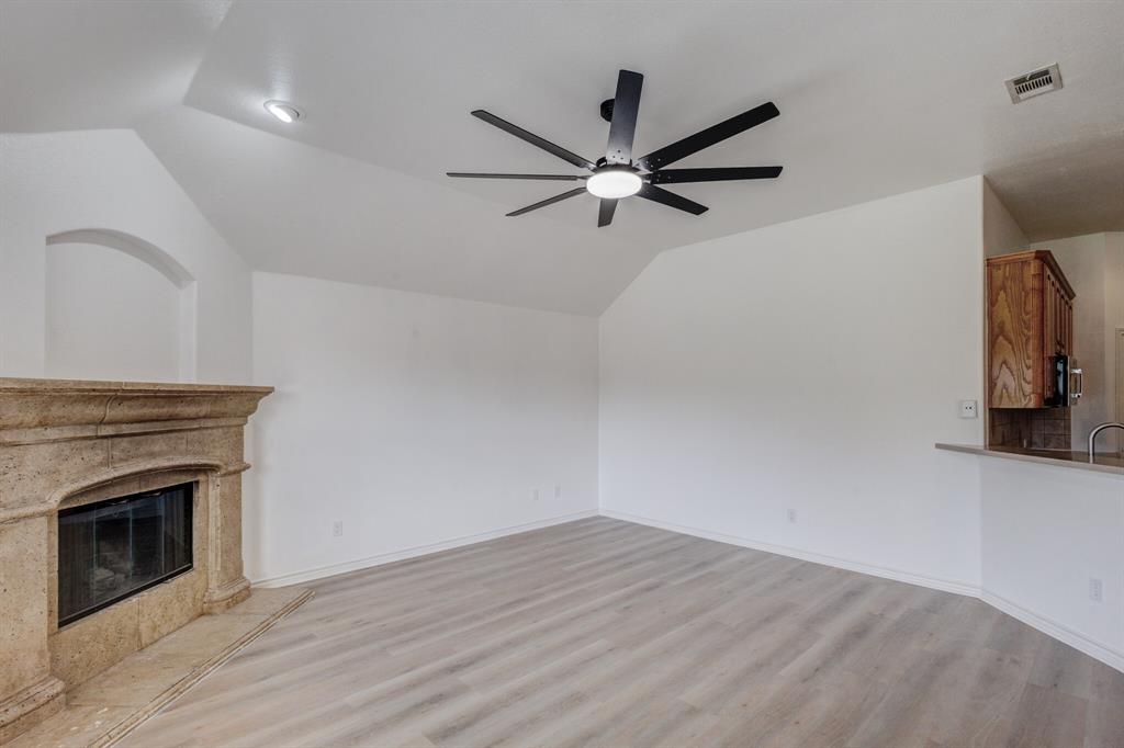 12405 Ark Road Frisco, TX 75035 - Photo 28 of 34 Unfurnished living room with vaulted ceiling, a premium fireplace, a ceiling fan, and light wood-type flooring