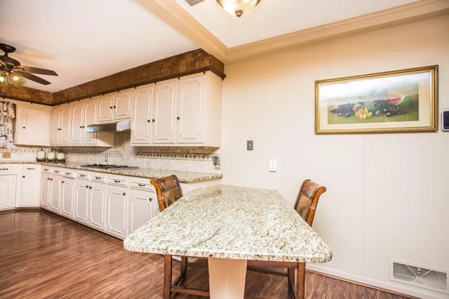 a kitchen with granite countertop a stove a sink dishwasher and white cabinets with wooden floor