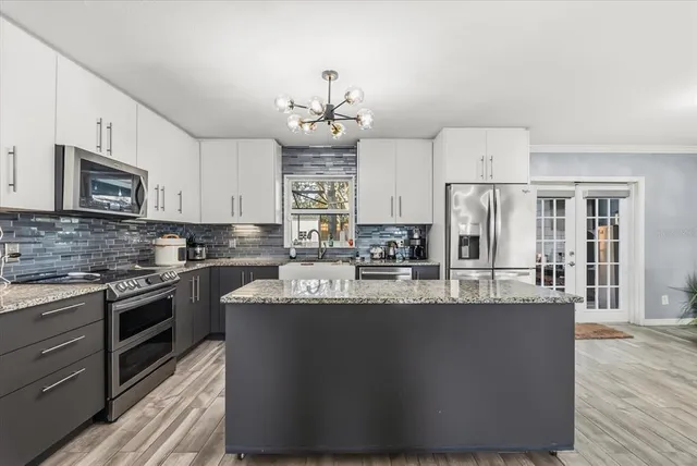 a large kitchen with stainless steel appliances granite countertop a stove a refrigerator a sink dishwasher a oven with white cabinets and wooden floor