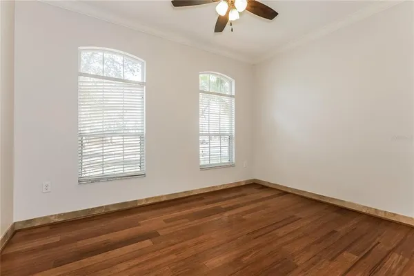 an empty room with wooden floor chandelier fan and windows