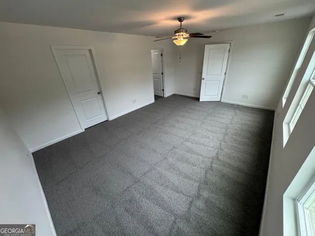 an empty room with chandelier fan and windows