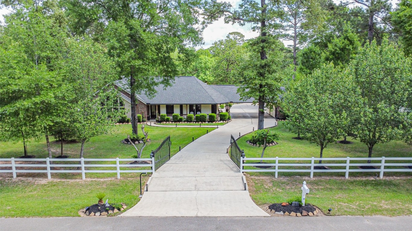 6002 Ranch Park Road Magnolia, TX 77354 - Photo 1 of 49 Welcome to 6002 Ranch Park Dr! A ranch-style home nestled among mature trees with a welcoming driveway and manicured lawn. The property features a white fence, landscaped gardens, and a serene, private setting. Ideal for those seeking a peaceful retreat.