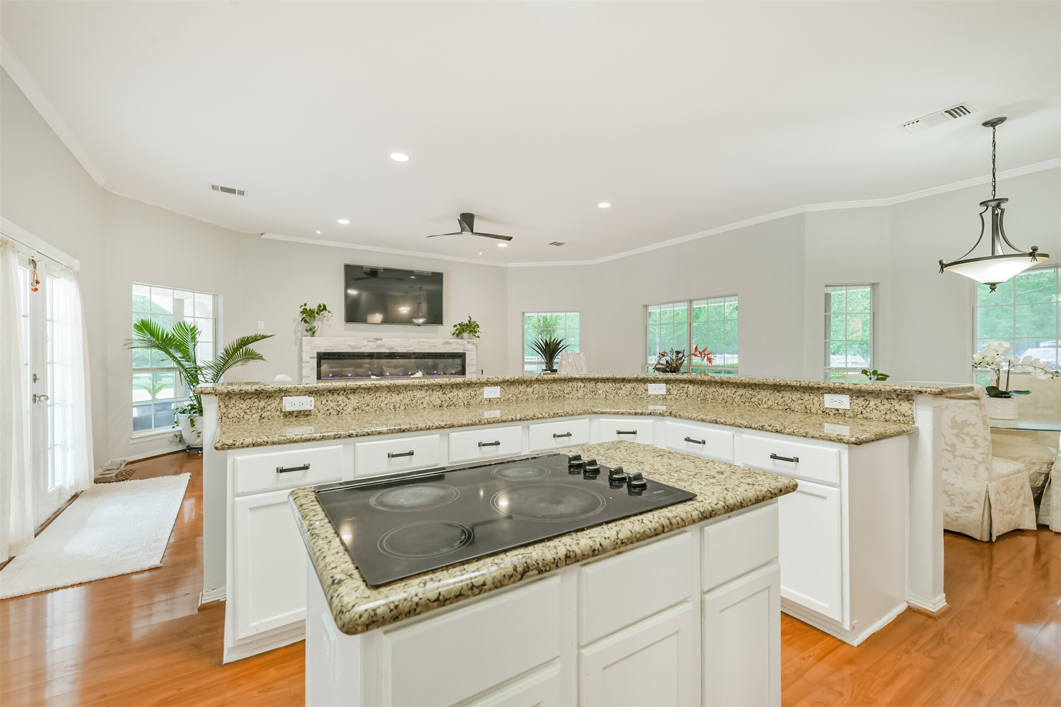 6002 Ranch Park Road Magnolia, TX 77354 - Photo 12 of 49 This open-concept living space features a modern kitchen with granite countertops and a center cooktop, overlooking the living area with a fireplace and large windows for natural light and access to an outdoor area through glass doors.