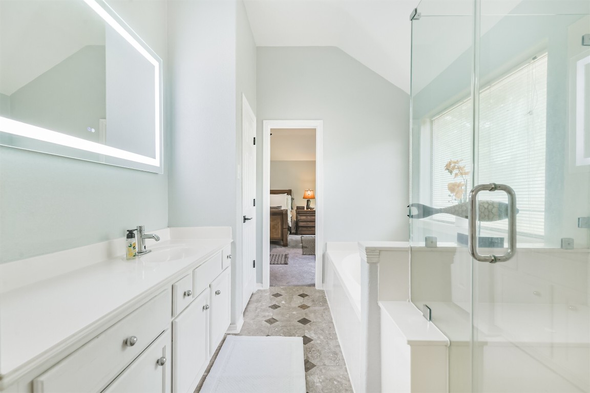 6002 Ranch Park Road Magnolia, TX 77354 - Photo 18 of 49 This photo showcases a bright, modern bathroom featuring a glass-enclosed shower, a sleek vanity with ample storage, and a large illuminated mirror. The space leads into a bedroom, creating a seamless flow between the two areas.