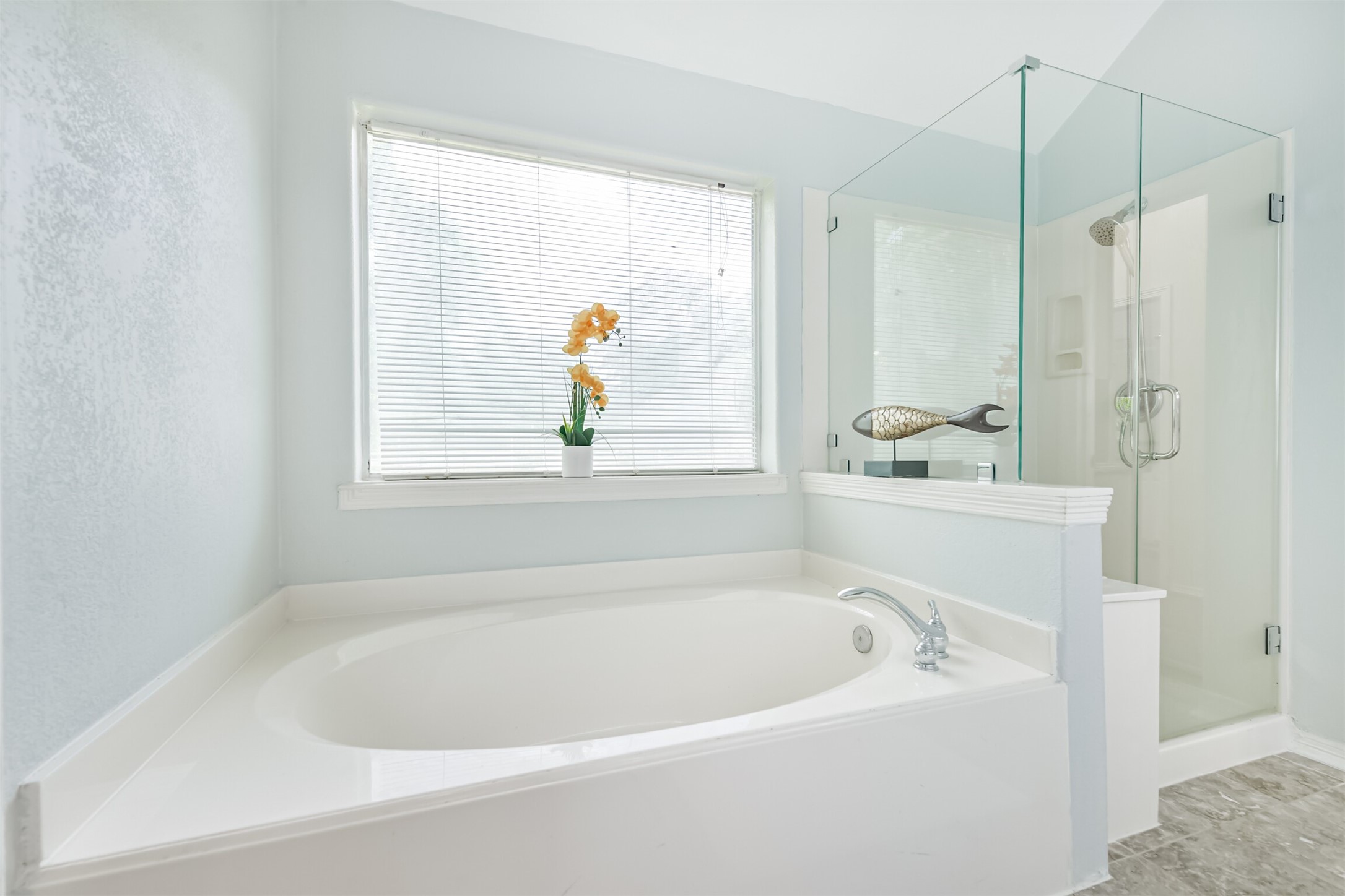 6002 Ranch Park Road Magnolia, TX 77354 - Photo 19 of 49 This bathroom features a large soaking tub next to a window with blinds, offering natural light. Adjacent is a modern glass-enclosed shower, creating a bright, open space ideal for relaxation.