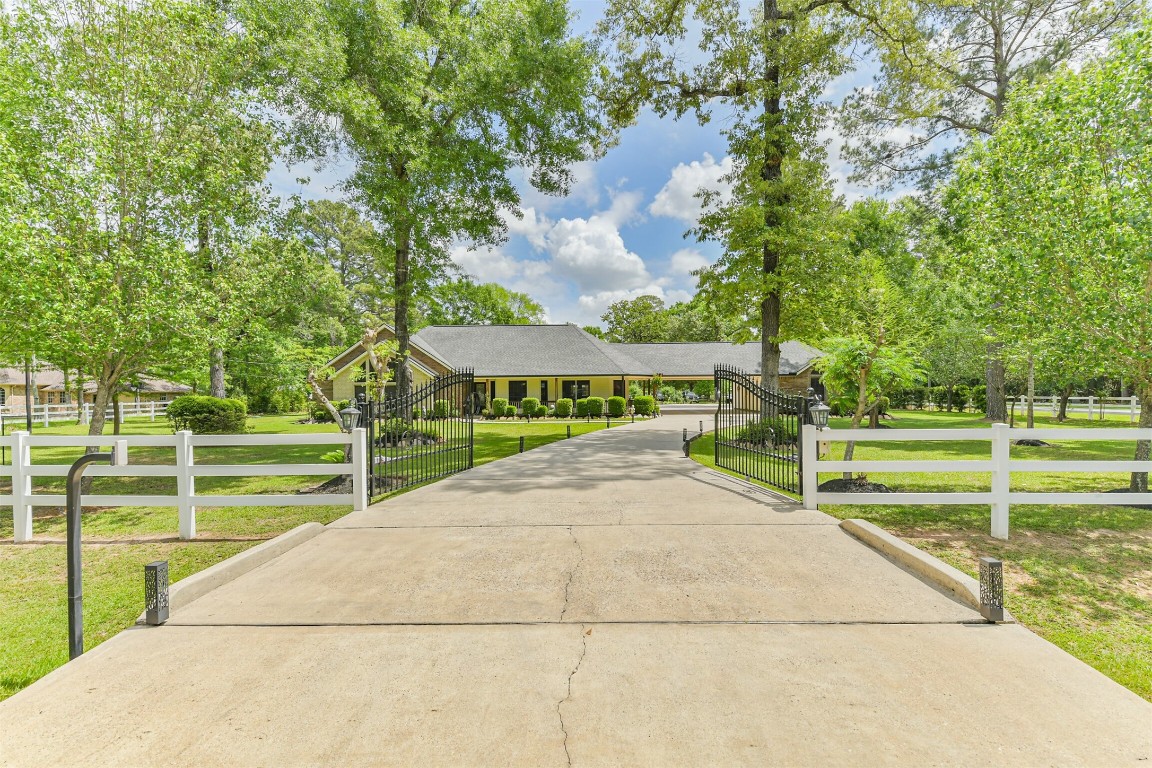 6002 Ranch Park Road Magnolia, TX 77354 - Photo 2 of 49 Stunning 2.9-acre home nestled in a lush, green setting. The property features a long, paved driveway leading to a gated entrance, surrounded by well-maintained landscaping and mature trees. A white picket fence adds a touch of elegance to the spacious front yard, creating a welcoming and serene atmosphere.