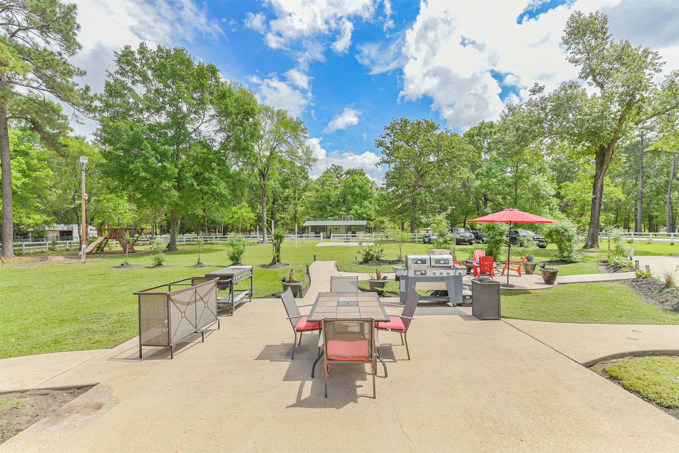 6002 Ranch Park Road Magnolia, TX 77354 - Photo 36 of 49 This photo showcases a spacious outdoor area with a large patio featuring dining furniture and a grill, surrounded by lush greenery and mature trees, perfect for entertaining or relaxing in a serene setting.