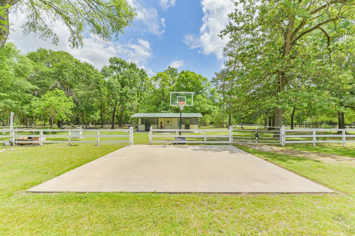 6002 Ranch Park Road Magnolia, TX 77354 - Photo 37 of 49 Expansive outdoor area featuring a basketball court, surrounded by lush greenery and mature trees, with a fenced perimeter.