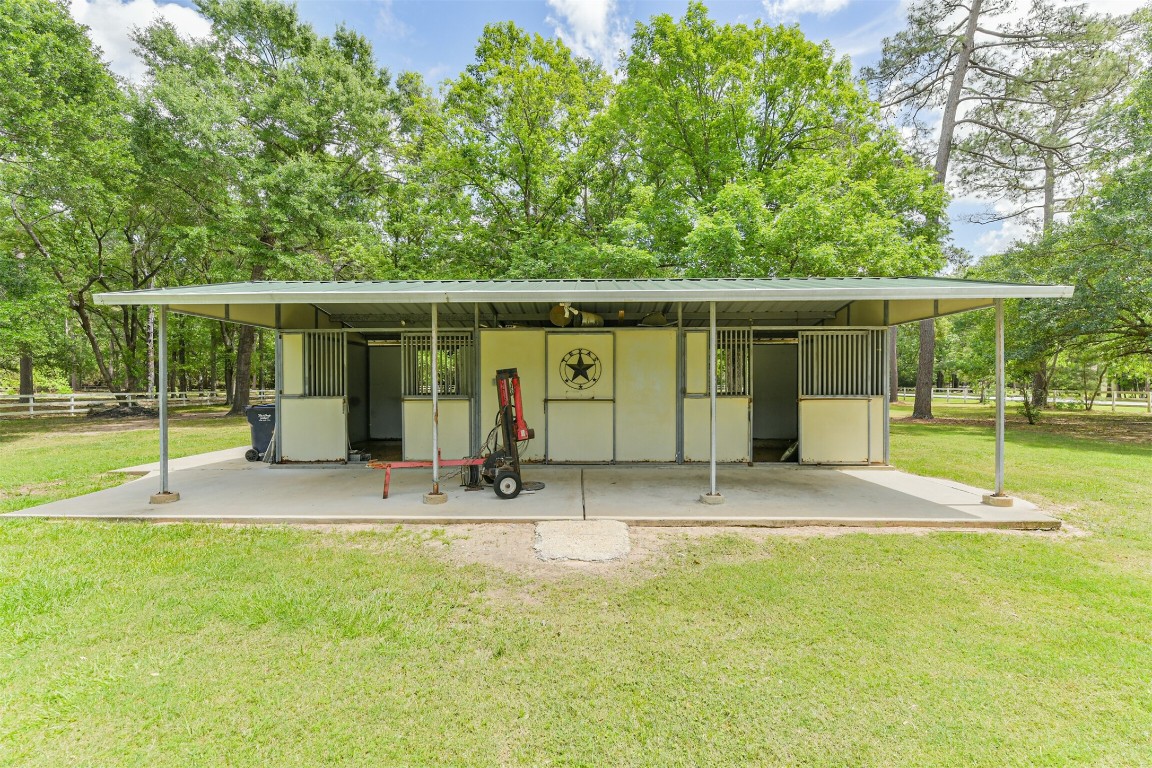 6002 Ranch Park Road Magnolia, TX 77354 - Photo 38 of 49 This photo features a 37x22 two-stall horse barn set on a concrete slab amidst a lush, green landscape. It's surrounded by mature trees, providing a serene and private setting. Ideal for equestrian enthusiasts.