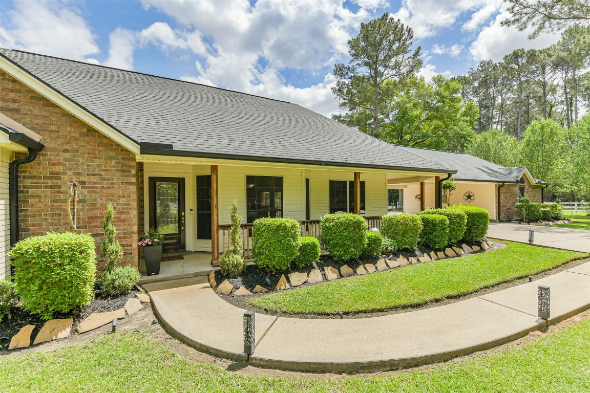 6002 Ranch Park Road Magnolia, TX 77354 - Photo 4 of 49 This charming home features a welcoming front porch, well-maintained landscaping, and a spacious driveway. The exterior combines brick and siding, surrounded by lush greenery and mature trees, creating a serene and inviting atmosphere.