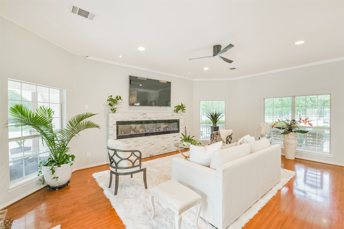 6002 Ranch Park Road Magnolia, TX 77354 - Photo 5 of 49 Bright and spacious living room with large windows, wood floors, and a modern fireplace. Features High ceiling, Recessed lighting, and ample seating. Decorated with lush plants, creating a welcoming atmosphere.