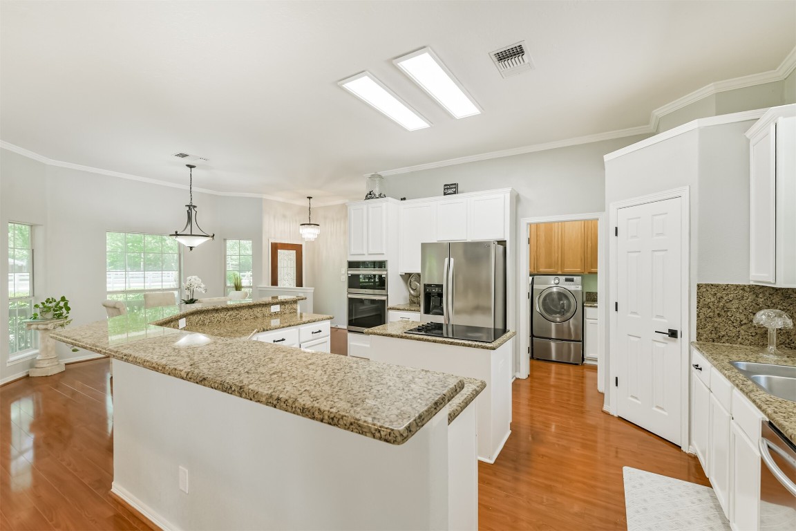 6002 Ranch Park Road Magnolia, TX 77354 - Photo 8 of 49 The kitchen features granite countertops, white cabinetry, and stainless steel appliances, creating a modern and inviting space. It opens to a well-lit dining area with large windows.