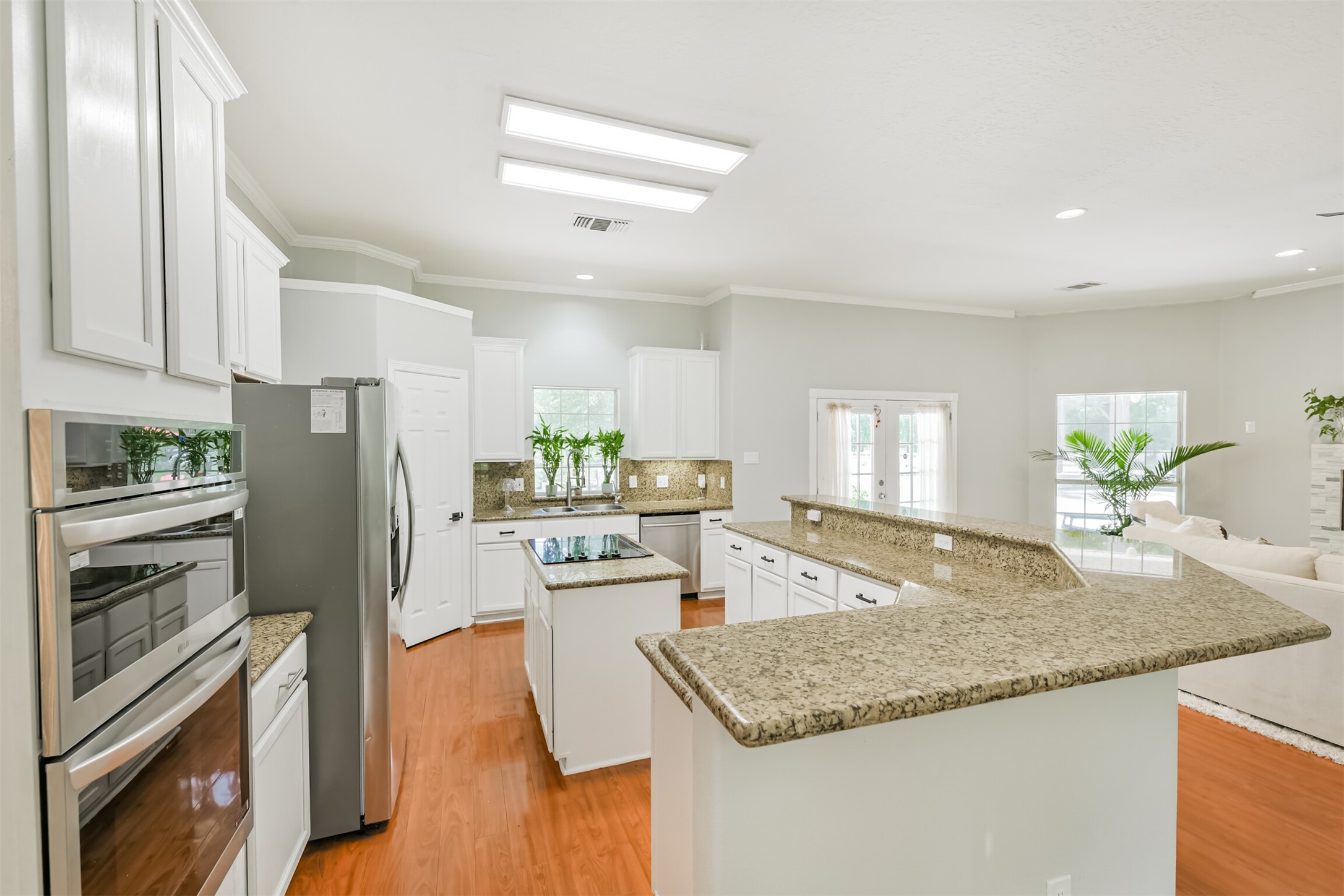 6002 Ranch Park Road Magnolia, TX 77354 - Photo 9 of 49 Bright, spacious kitchen with granite countertops, white cabinetry, and stainless steel appliances. Open layout connects to a living area, featuring hardwood floors and ample natural light.