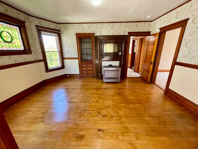 a view of an empty room with window and hardwood floor