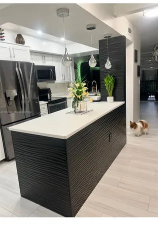 a room with stainless steel appliances kitchen island granite countertop a sink a counter space and cabinets