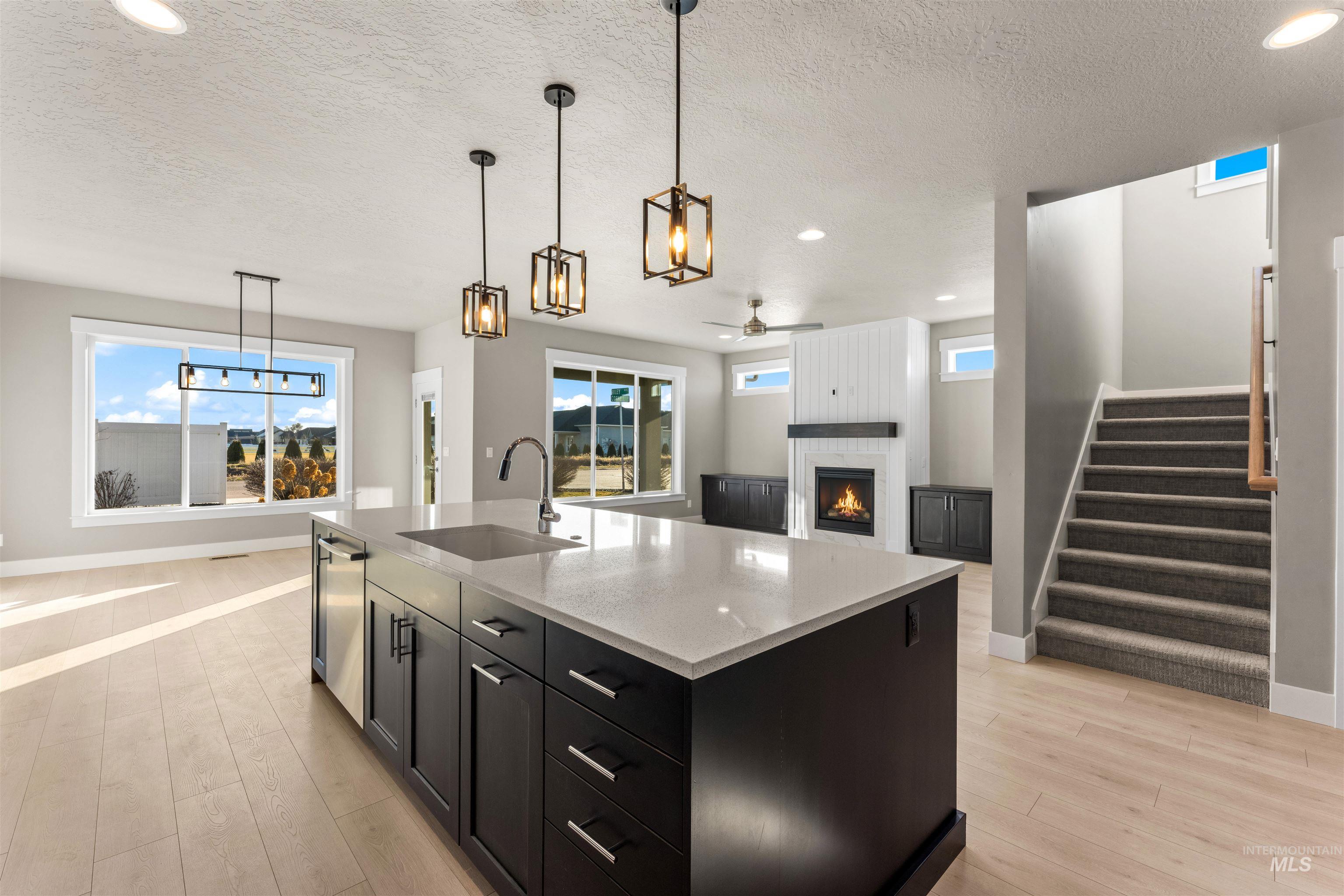 8097 Tandy Cove Street Middleton, ID 83644 - Photo 13 of 37 Kitchen featuring dark cabinets, decorative light fixtures, ceiling fan, a kitchen island with sink, and a fireplace