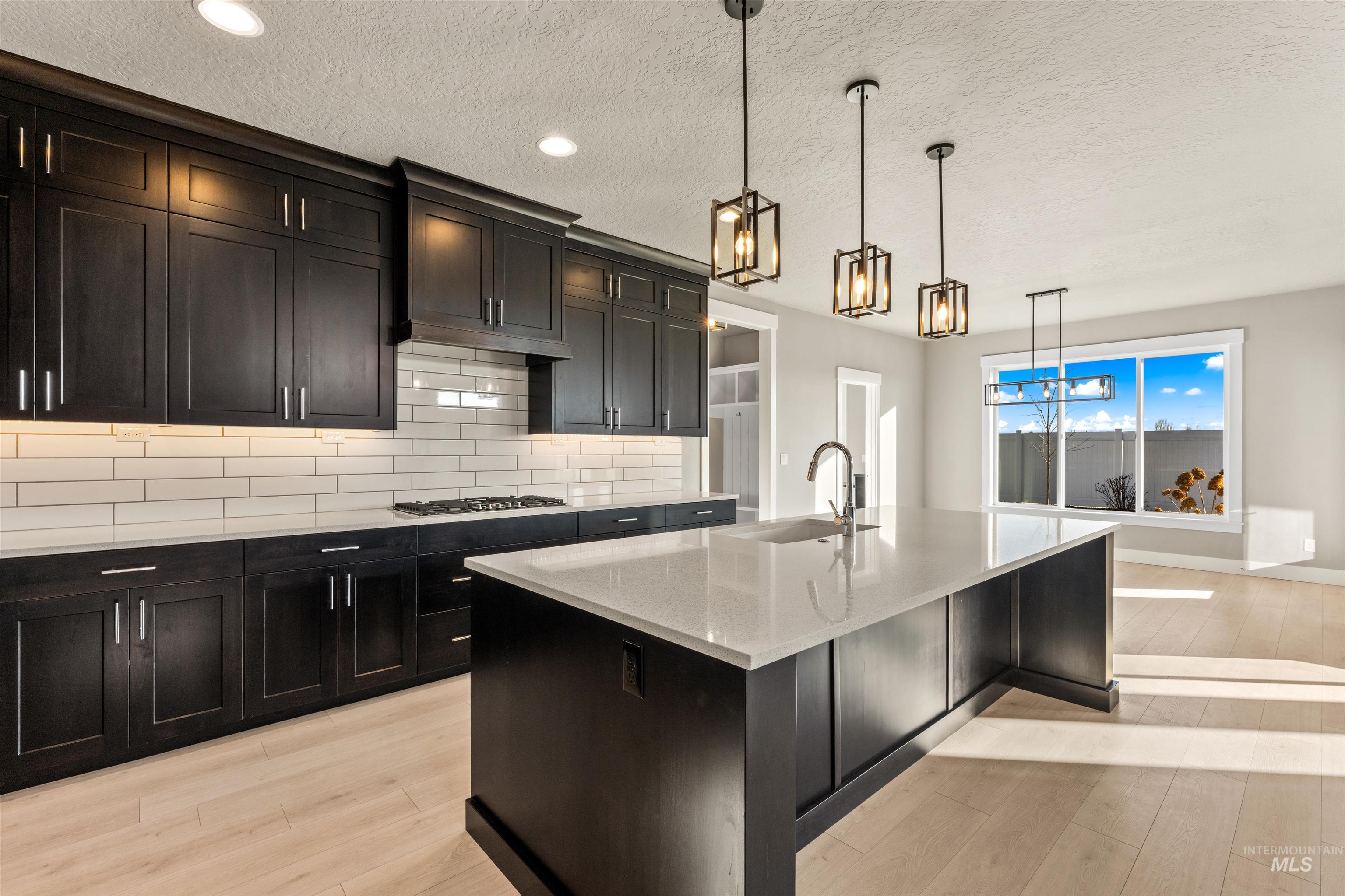8097 Tandy Cove Street Middleton, ID 83644 - Photo 14 of 37 Kitchen featuring light stone countertops, light wood-style floors, backsplash, hanging light fixtures, and a textured ceiling