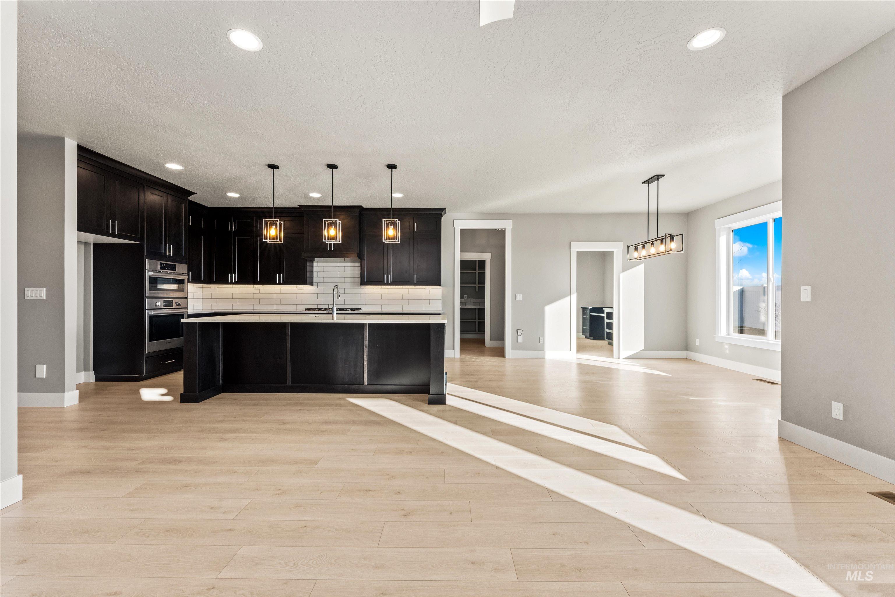 8097 Tandy Cove Street Middleton, ID 83644 - Photo 37 of 37 Kitchen with open floor plan, hanging light fixtures, a kitchen island with sink, dark cabinets, and backsplash