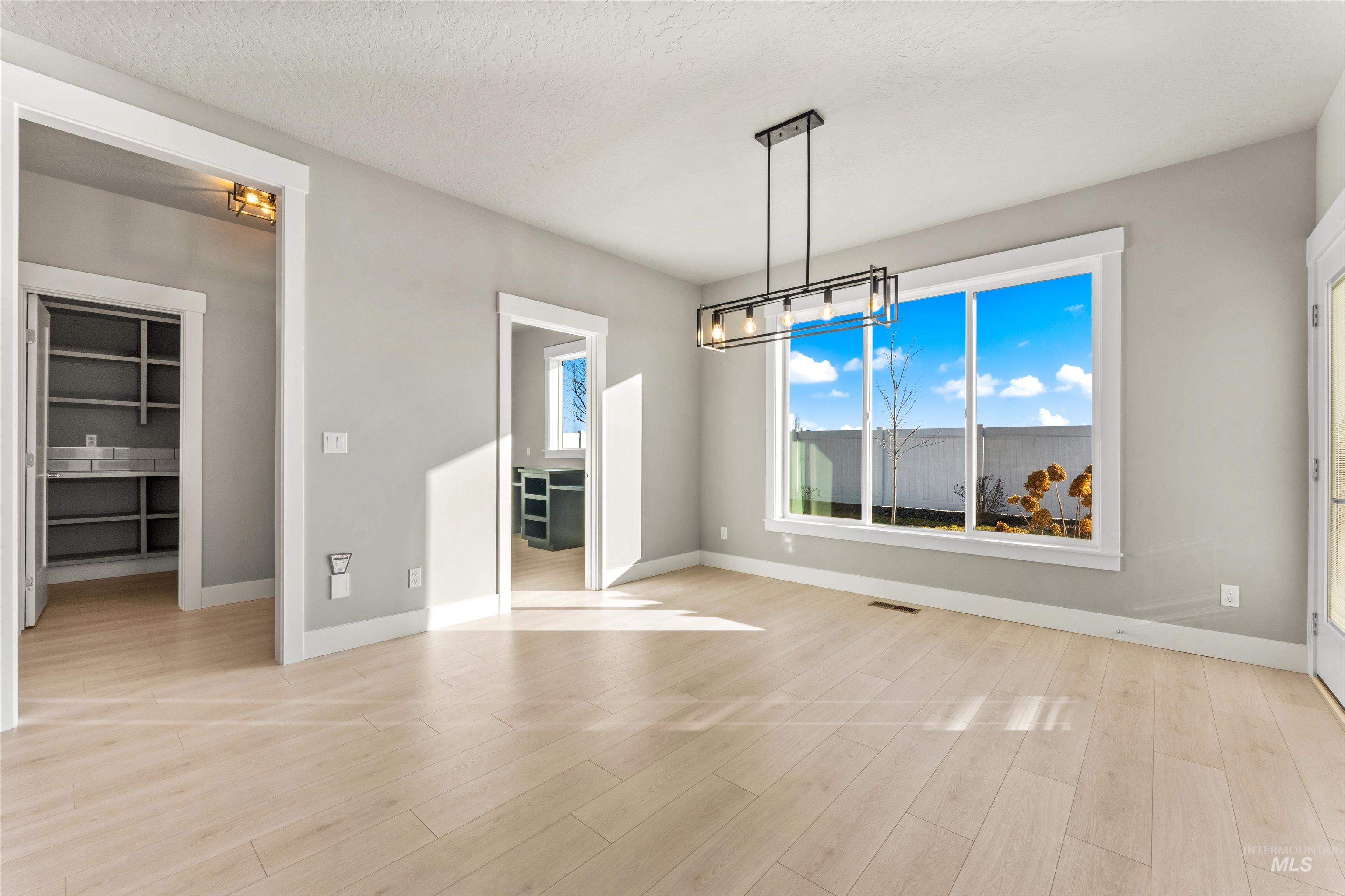 8097 Tandy Cove Street Middleton, ID 83644 - Photo 8 of 37 Unfurnished dining area with light wood-style flooring, suspended lighting, and a textured ceiling