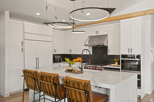 4499 North Seven Bridges Road, Unit 9 Eden, UT 84310 - Photo 8 of 65 White shaker-style cabinetry with matte black hardware, integrated refrigerator, stainless steel range hood, built-in double oven, and a kitchen island with a light-toned countertop