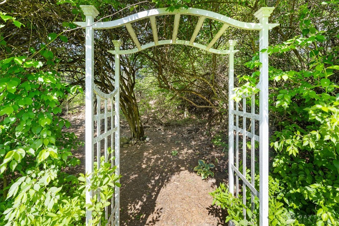 841 Willow Road Springfield, OH 45502 - Photo 46 of 64 Enter a serene outdoor space through a charming white arbor, surrounded by natural foliage.