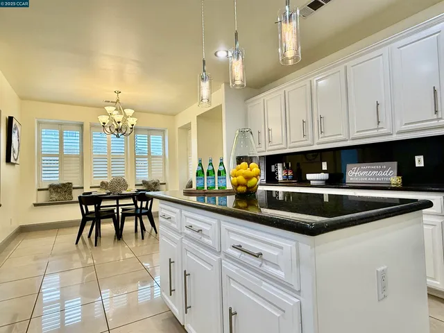 a kitchen with stainless steel appliances granite countertop a sink a stove top oven a dining table and chairs with white cabinets