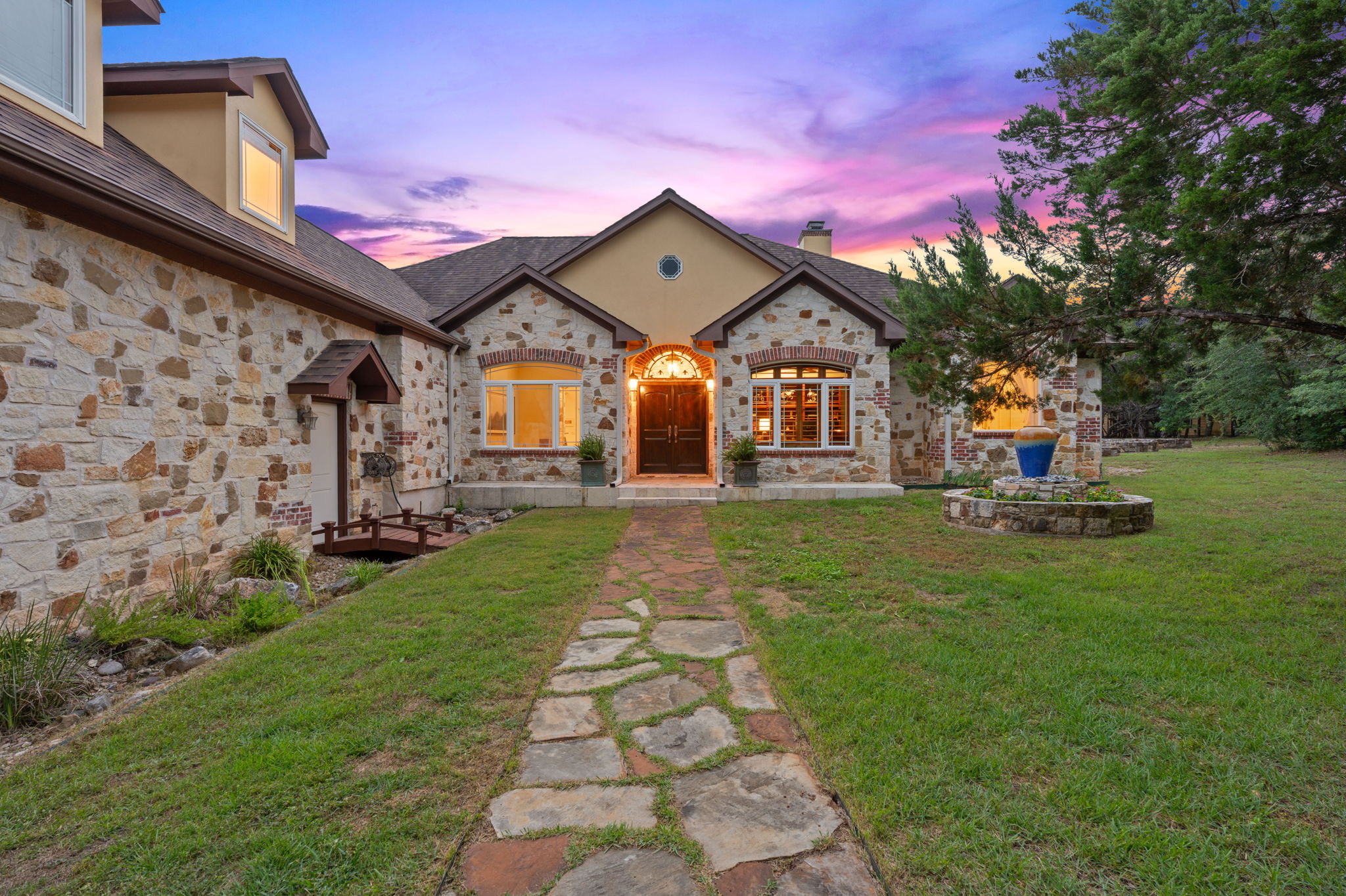 8121 Bluff Trail Austin, TX 78737 - Photo 1 of 40 A dramatic sunset illuminates the handsome stone and stucco facade of this welcoming residence, complemented by a charming stepping stone pathway.