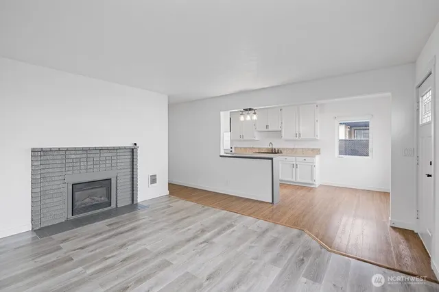 a view of a kitchen and an empty room with wooden floor and a fireplace