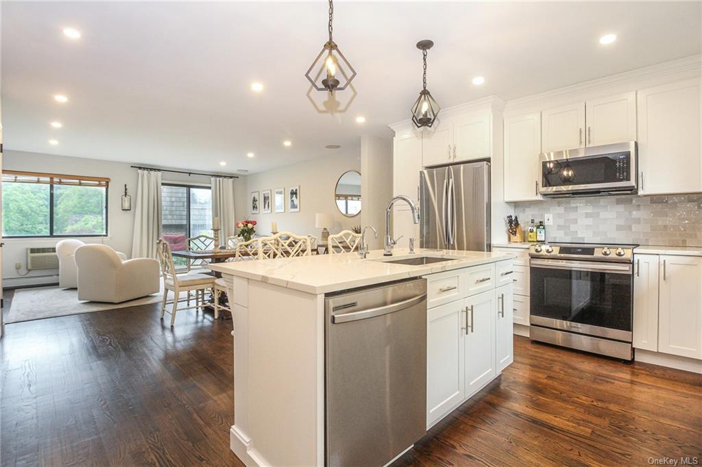 a kitchen with stainless steel appliances a stove a sink a kitchen island with furniture and wooden floor
