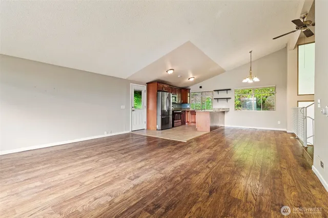 a view of an empty room and kitchen with wooden floor