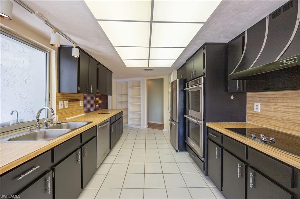 379 Torrey Pines Point Naples, FL 34113 - Photo 8 of 21 Galley kitchen featuring wood-finish countertops, black cabinetry with silver hardware, stainless steel appliances, and a dual basin sink