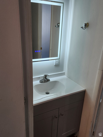 332 Joshua Street Tooele, UT 84074 - Photo 8 of 16 Vanity area featuring an illuminated rectangular mirror, a chrome-finish single-handle faucet, and a contemporary gray two-door cabinet