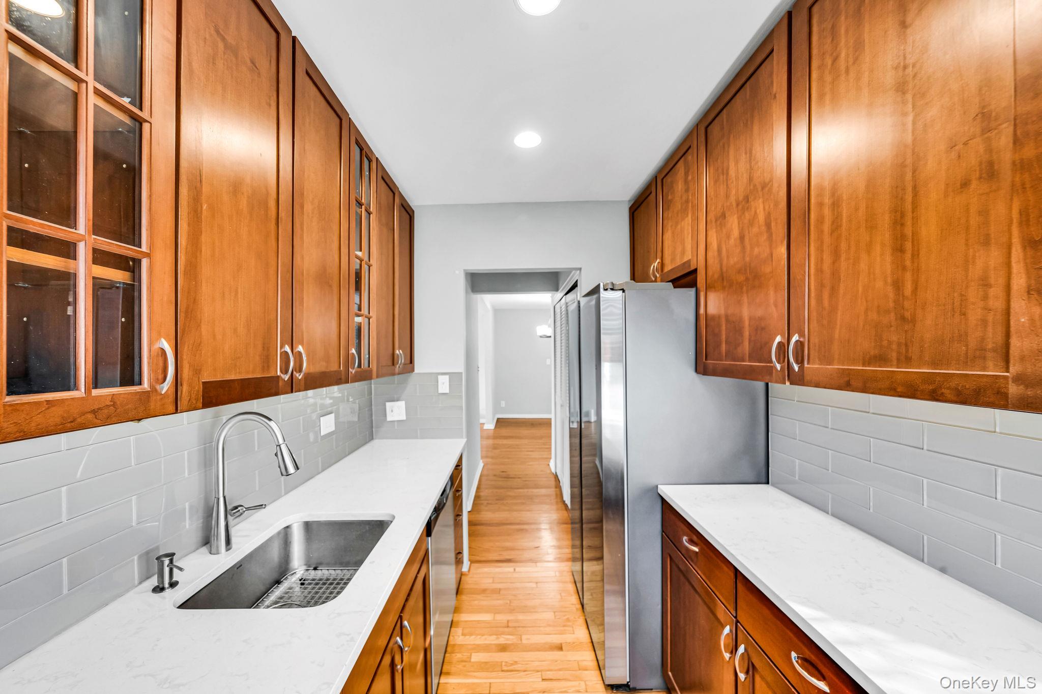 213-05 75th Avenue, Unit 4N Queens, NY 11364 - Photo 13 of 19 Kitchen featuring brown cabinetry, light stone counters, glass insert cabinets, light wood-style floors, and appliances with stainless steel finishes