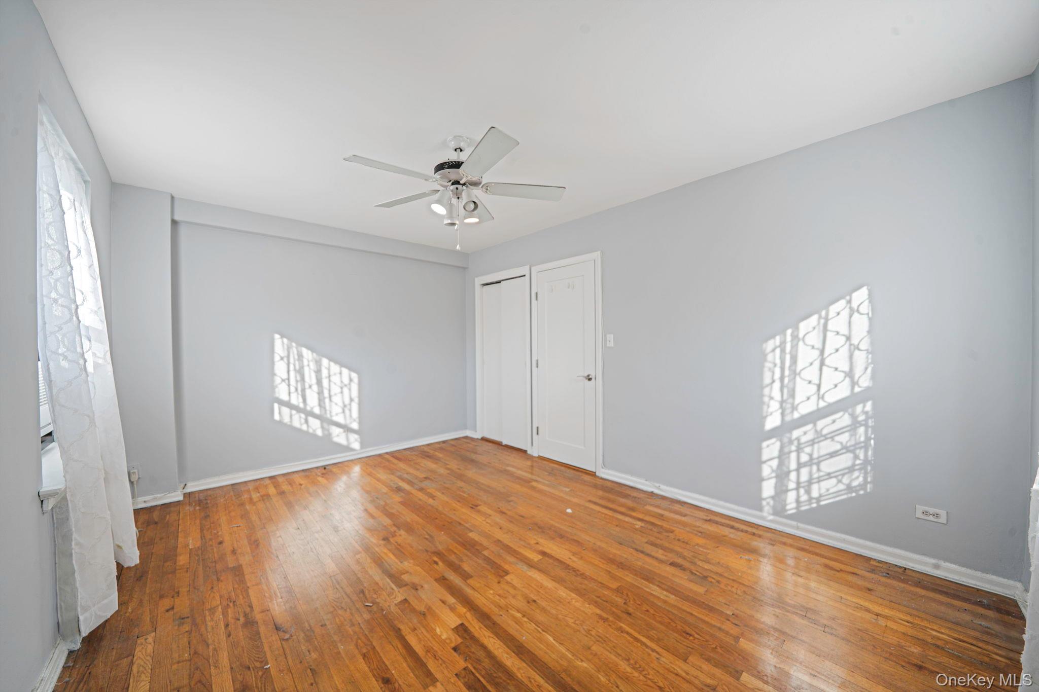 213-05 75th Avenue, Unit 4N Queens, NY 11364 - Photo 10 of 19 Unfurnished bedroom featuring multiple windows, wood-type flooring, and a ceiling fan