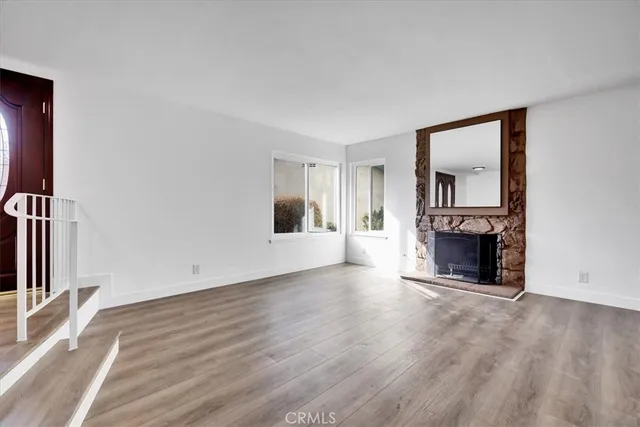 an empty room with wooden floor fireplace and windows