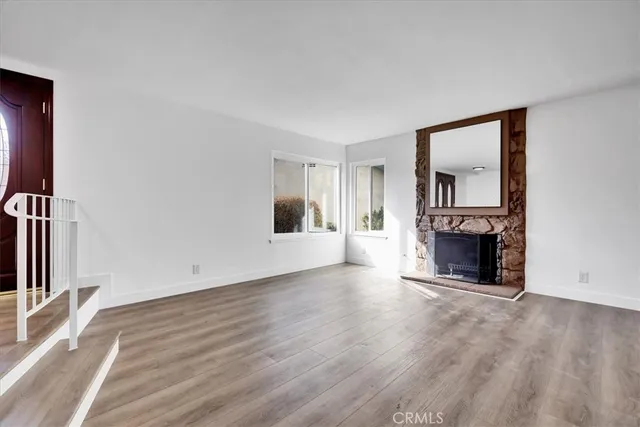 an empty room with wooden floor fireplace and windows